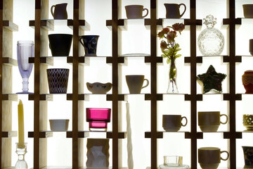 Various items are placed on a shelf with a contour light at the back. Silhouettes of dishes, candles in candlesticks, decorative elements.
