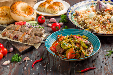 dishes of Uzbek cuisine lagman, pilaf, skewers of lamb, bread and vegetables on old wooden table