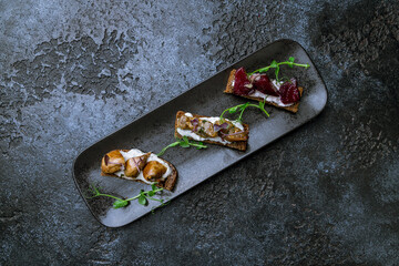 assorted bruschett on black plate on dark stone table top view