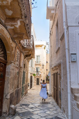 Blonde girl walking near baroque building in Polignano a Mare, Bari, Puglia, Italy.