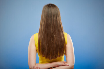 Obraz premium Woman in yellow casual dress standing back with long hair. Isolated female portrait on blue background.