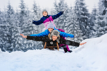 Fototapeta na wymiar Happy family father, daughter and son are sledding in snow. Happy winter holidays.