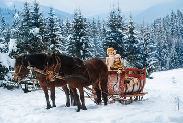 Fototapeta na wymiar Two children ride on a retro sleigh with horses in winter time. Mountain snowy landscape background. Tours, horse riding.