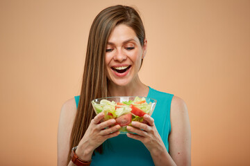 Smiling woman looking in salad bowl, isolated portrait on yellow brown background.