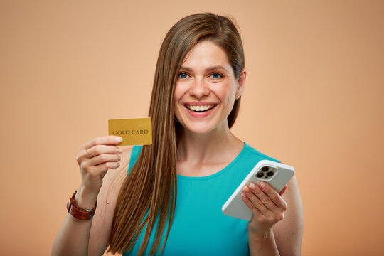 Smiling woman holding credit card and smartphone, isolated portrait on yellow brown background.