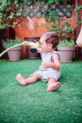 Toddler playing in the garden of his house with a hose to water the plants