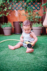 Toddler playing in the garden of his house with a hose to water the plants