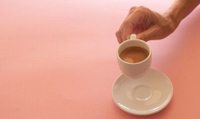 Woman's hand picking up white cup with coffee on light pink background