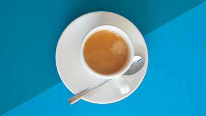 White cup with coffee and a metal spoon on a bicolor blue background