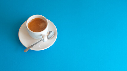 White cup with coffee and a shiny metal spoon on a blue background