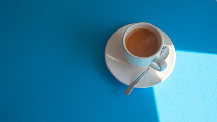 White cup with coffee and a shiny metal spoon on a blue background