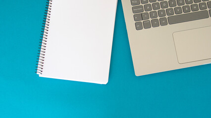 Blank page of a notebook next to a laptop on a blue background