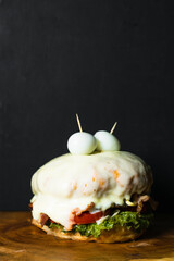 Colombian hamburger dipped in melted cheese, served on a wooden tray or plate, on a black background with space for copying text. street food