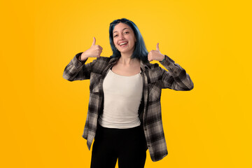 Smiling young woman student with blue hair doing positive gestures with her hands isolated over yellow background - 525699896