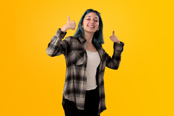 Smiling young woman student with blue hair doing positive gestures with her hands isolated over yellow background - 525700061