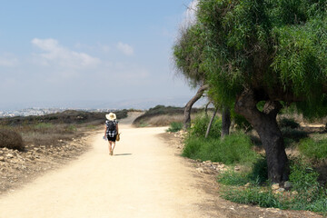 Girl in a hat on a sandy road. Archaeological area, Cyprus. Desert road and green trees. The man on the road.
