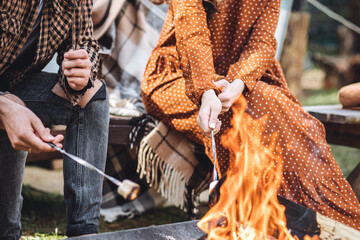Young beautiful loving couple travelling across country in the van. Millennial man and woman in a travel camper. Cozy atmosphere, vacations vibe. Drinking tea, cooking marshmallow on a campfire