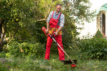 Mowing grass with electric lawn mower. Garden work concept. Man mows the grass with hand mower in...