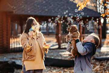 Happy family mother and teen boy son with cute cocker spaniel puppy blow soap bubbles outdoor in autumn park.