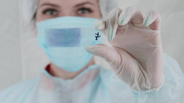 A laboratory technician in special clothes and a mask on his face shows an object stack. A female laboratory assistant in the laboratory conducts an analysis in a protective mask. Health care concept