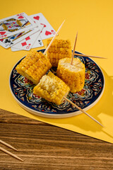 
corn on skewers on a ceramic plate. Back yellow background and playing cards