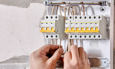 An electrician connects wires to fuse box in consumer unit of electrical panel.