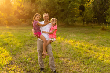 Happy family in outdoor park at sunny day. Dad and two daughters in the green garden. Group of people on green grass.