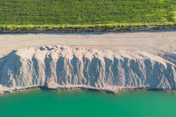 Landfill of the mined white fine aggregate between the turquoise lake and the farmland. Background....