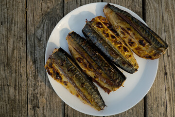 Four mackerel prepared on a grill in nature on a white plate. Selective focus. Top view. Wooden background.