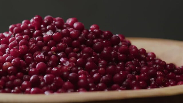 Big wooden plate of tasty red frozen cranberries at gray background
