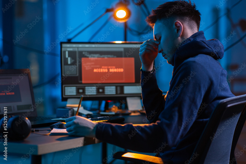 Poster cybercrime, hacking and technology concept - male hacker in dark room writing to notebook and using 