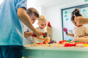 Relaxing sensory play with moldable kinetic sand at nursery school. Toddlers with their teacher...