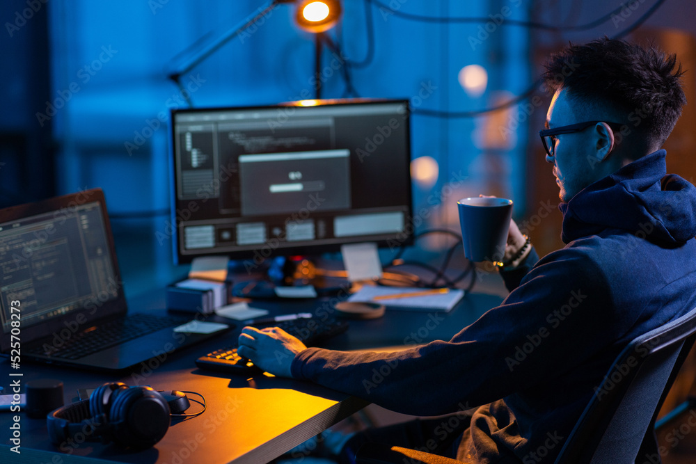 Poster cybercrime, hacking and technology concept - male hacker in dark room drinking coffee and using comp
