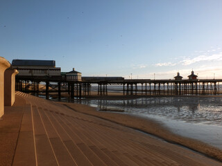 Naklejka premium the seawall and steps on blackpool beach at sunset with the north pier reflected on the beach