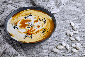 A plate of creamy pumpkin soup with cream and black cumin and pumpkin seeds on a light knitted wool...