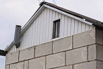 white plastic attic with one window on a gray brick wall of a private house against the sky