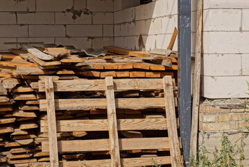 one brown wooden pallet stands by a pile of planks outdoors against a white brick wall of a building