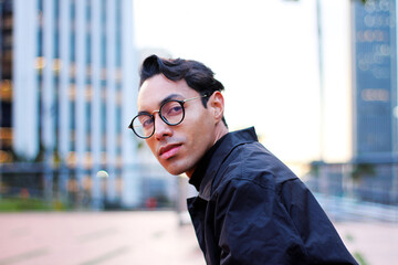 serious young man with glasses looking at camera in front of buildings as business person