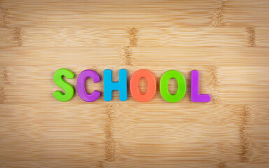 The word school is laid out of multicolored letters on a table background with a wood texture. Concept. School