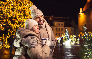 people, holidays and leisure concept - happy couple with tea cups over christmas lights in city at...
