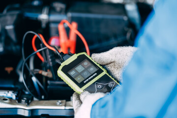 close up view of automotive mechanics repairman using a digital battery tester to check and analyze the battery in the car, check the mileage of the car, auto maintenance service concept.