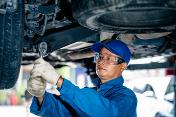Auto mature mechanic repairman in uniform using a socket wrench working auto suspension repair in...