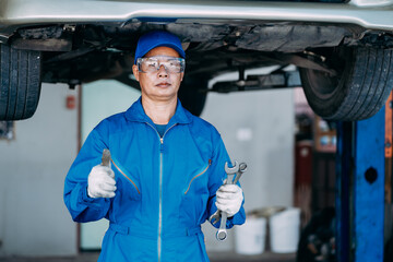 Auto mature mechanic repairman in uniform thumbs up and holding wrench looking confident in the garage, positive thinking, repair and maintenance service concept.