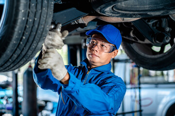 Auto mature mechanic repairman in uniform using a socket wrench working auto suspension repair in...