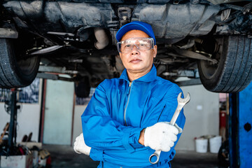 Auto mature mechanic repairman in uniform thumbs up and holding wrench looking confident in the...