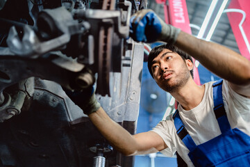 Young auto mechanic repairman in uniform repairing car brake systems and suspension in the garage,...