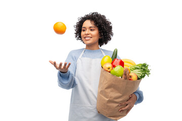 cooking, delivery and people concept - happy smiling woman in apron holding takeaway food in paper bag and throwing orange in air over white background