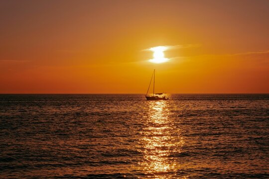 Beautiful Sunset Over The Ocean With Yellow Sky And A Boat Sailing On Th Water