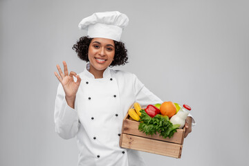 cooking, culinary and people concept - happy smiling female chef in toque holding food in wooden box and showing ok gesture over grey background