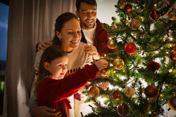 family, winter holidays and people concept - happy mother, father and little daughter decorating christmas tree at home